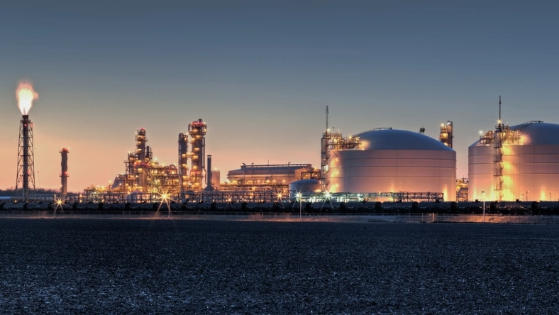 Industrial energy facility with storage tanks and flare stack at dusk