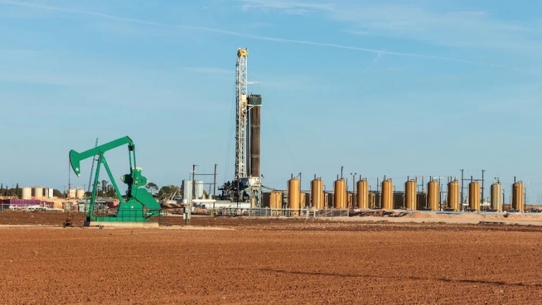 Oil pumpjack and drilling rig at onshore shale production site